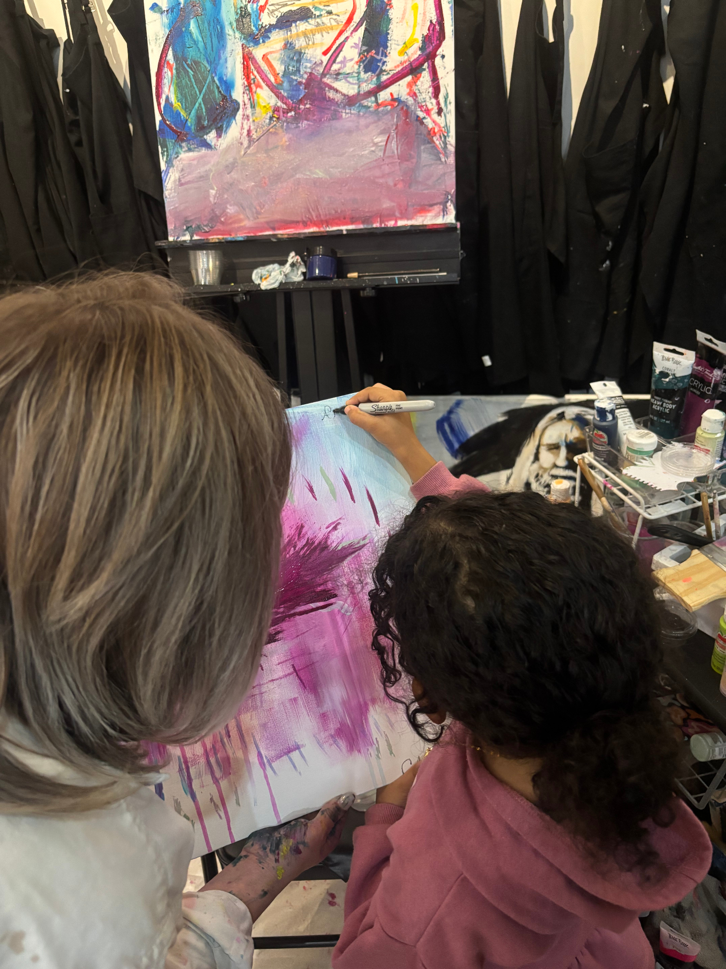 Amillie signing her canvas in the studio with her teacher