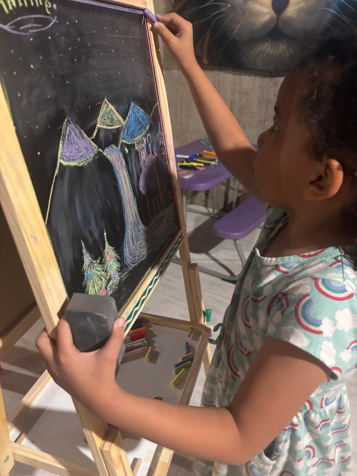 Amillie drawing a colorful castle on a chalkboard easel